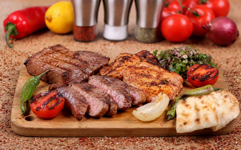Grilled meat served with vegetables on a wooden board.