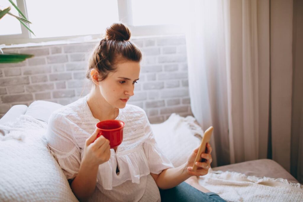 Woman looking at her phone while sitting with a drink, representing how social media can create unrealistic weight loss expectations and discourage healthy habit building