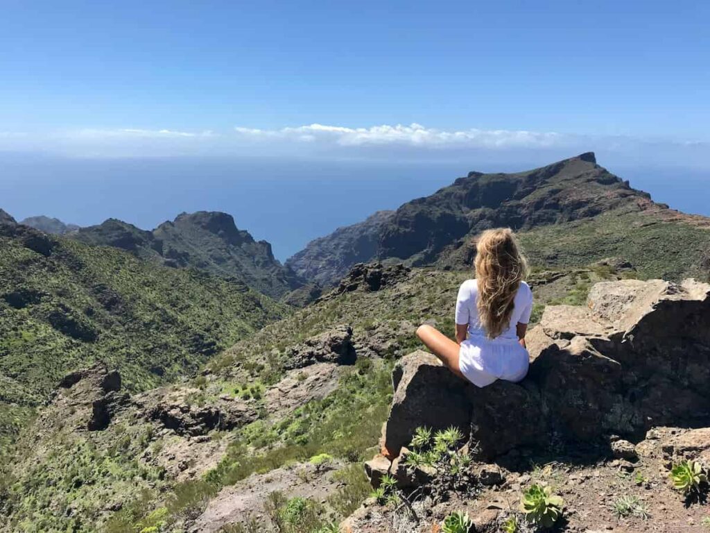 Woman sitting on a mountain overlooking a wide landscape, representing how self-acceptant and a positive mindset can support a healthier and more sustainable weight loss journey