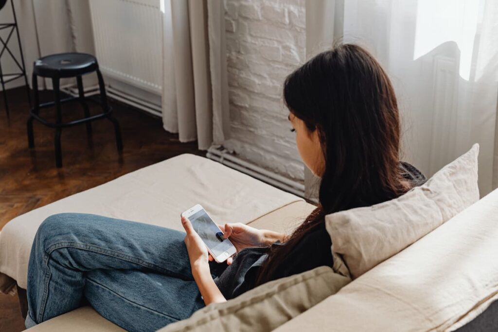 A person sitting on a couch scrolling on a smartphone at home.