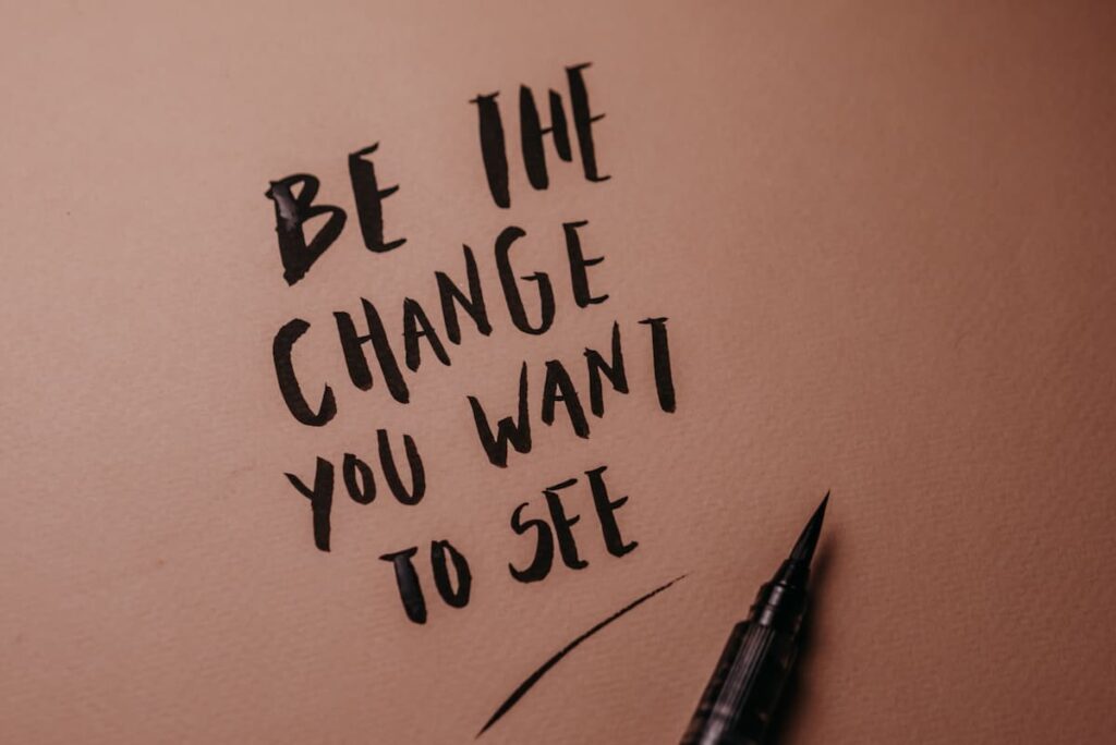 Handwritten quote saying "Be the change you want to see" beside a black pen