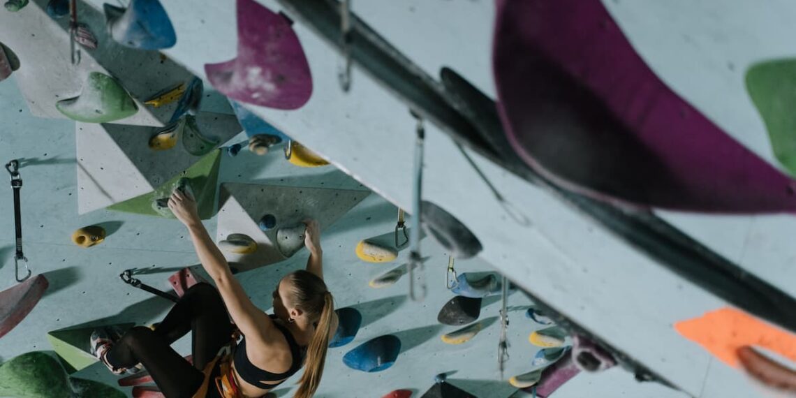 A woman climbing an indoor rock wall, looking for the next possible hold to continue moving forward.