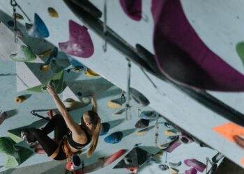A woman climbing an indoor rock wall, looking for the next possible hold to continue moving forward.